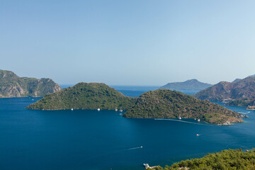 Fototapeta na wymiar Marmaris, Turkey – Beautiful view of the islands and the crystal clear water of the bay at sunny day with its misty green mountains at background and the blue bay.