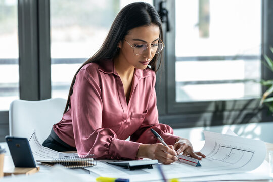 Concentrated young business woman working with blueprint in the office.