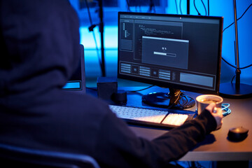 cybercrime, hacking and technology concept - close up of hacker in dark room drinking coffee and...