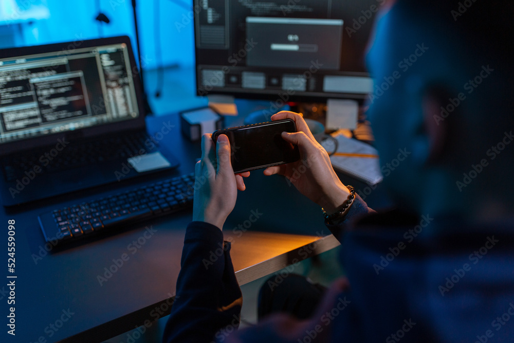 Poster cybercrime, hacking and technology concept - close up of male hacker with smartphone using computer 