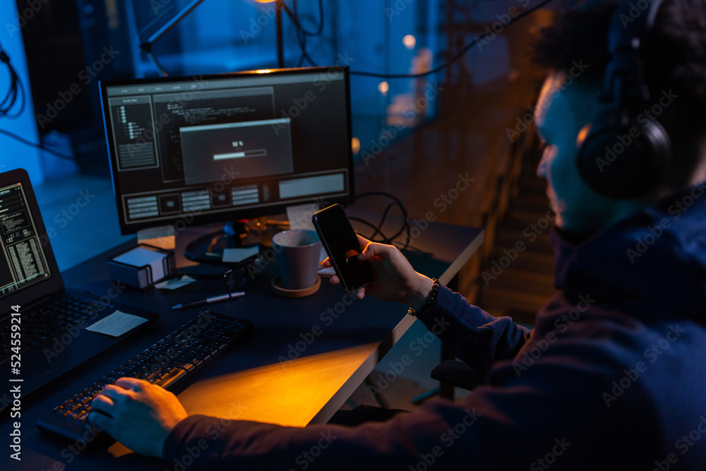 Poster cybercrime, hacking and technology concept - close up of male hacker with smartphone using computer 