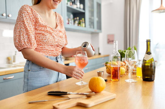 Drinks And People Concept - Close Up Of Woman Pouring Soda From Tin Can To Wine Glass And Making Orange Cocktail At Home Kitchen