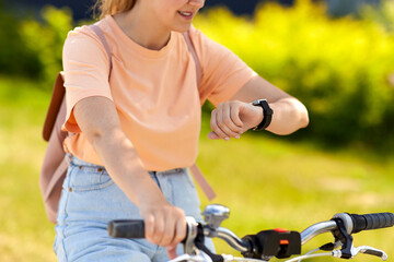 Fototapeta na wymiar people, leisure and lifestyle - close up of happy smiling woman with smart watch riding bicycle on city street