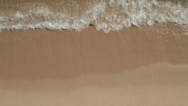 Top down ascending footage of crystal clear water on beach. Waves washing sand on coast. Barcelona, Spain
