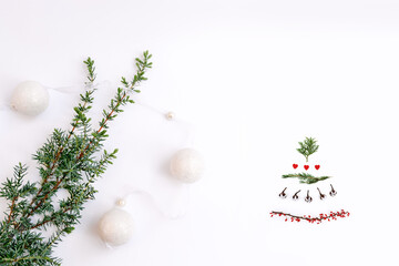 Fototapeta na wymiar Christmas creative tree and green twig with garland balls on white background as symbol of new year. Tree is made of twigs of thuja, cotton, red hearts and dogwood berries. Alternative beauty concept