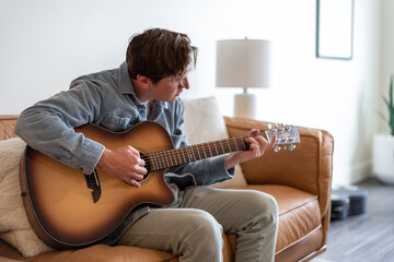 Young man sitting on the couch playing acoustic guitar