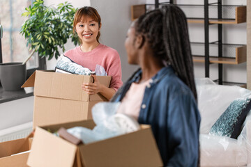 Fototapeta na wymiar moving, people and real estate concept - happy smiling women with boxes at new home