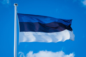 Close-up of flag of Estonia on blue sky background. Estonian flag waving in wind and sunlight. 
