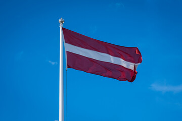 Flag of Latvia on blue  sky background. Latvian flag waving in wind.