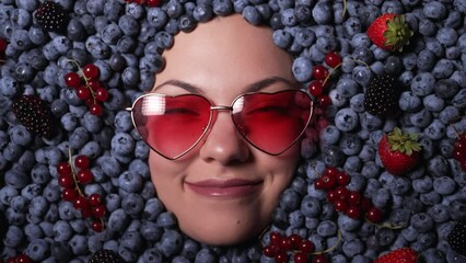 Happy woman face in eyewear fresh ripe berries - blueberries, strawberries, currant. Young girl covered with blackberry. Lady enjoying organic bilberry plant. Diet, antioxidant, healthy vegan food.