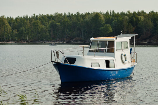 a small river boat is moored to the bank of the river, in the background is a green forest and the sky