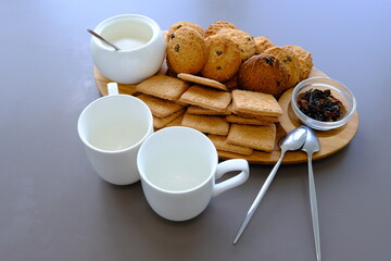 A tasty snack two cups of black tea and a plate of oatmeal cookies a wooden board on the gray background, leaf tea.