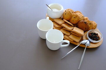 A tasty snack two cups of black tea and a plate of oatmeal cookies a wooden board on the gray background, leaf tea.