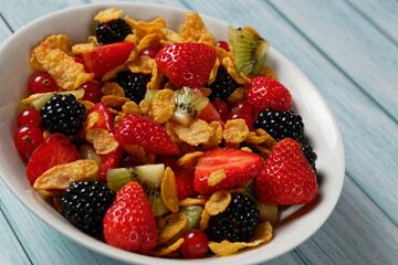 Corn flakes with berry fruits and kiwi, served in a bowl.