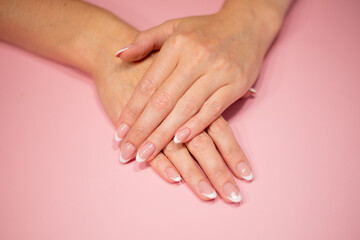 female hands with beautiful classic french white manicure. Fingers isolated on a pastel pink background.