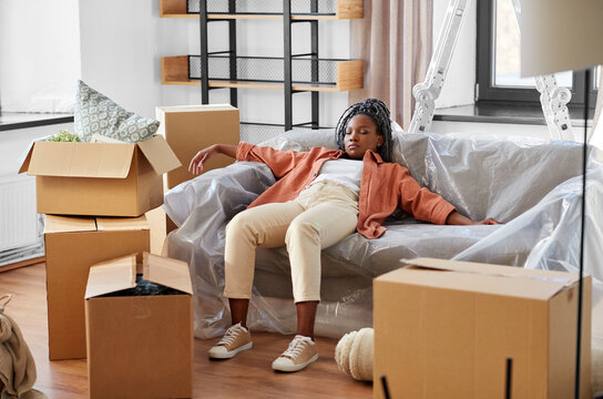 moving, people and real estate concept - tired woman with boxes sleeping on sofa at new home