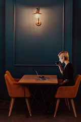Businesswoman sitting in coffee shop at wooden table, drinking coffee and using laptop. Businesswoman browsing internet, chatting, blogging. Selective focus 