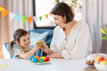 holidays, family and people concept - happy little baby daughter and mother tapping colored easter...