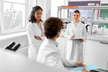 science research, work and people concept - international group of happy scientists with folder and clipboard working in laboratory