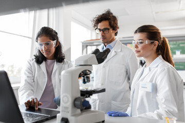 science research, work and people concept - international team of scientists with laptop computer and microscope working in laboratory