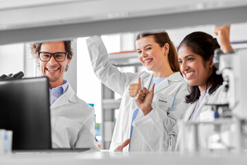 science, work and people concept - international group of happy scientists celebrating success and showing thumbs up in laboratory - Powered by Adobe