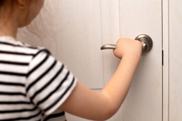 Girl stands near a closed door and holds the door handle. A child is alone at home in a dangerous situation. Girl opens the door to the room