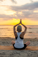 Fototapeta na wymiar yoga, mindfulness and meditation concept - woman meditating in lotus pose on beach over sunset