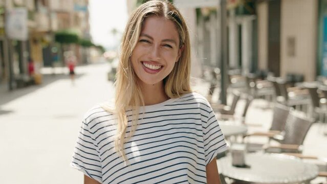 Young blonde woman smiling confident doing ok sign with thumbs up at street