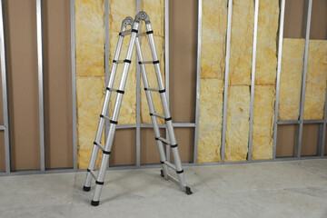 Ladder near wall with metal studs and insulation material indoors