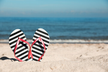 Naklejka premium Striped flip flops in sand on beach near sea. Space for text