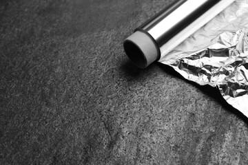 Roll of aluminum foil on grey table, closeup. Space for text