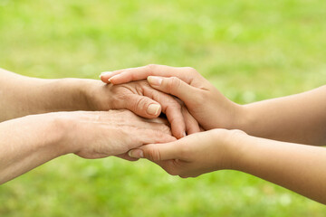 Young and elderly women holding hands outdoors, closeup