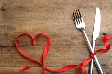 Cutlery set and red ribbon on wooden background, above view with space for text. Valentine's Day dinner