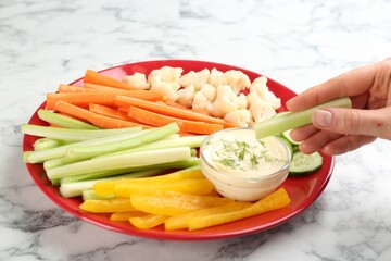 Woman dipping celery stick in sauce at white marble table, closeup