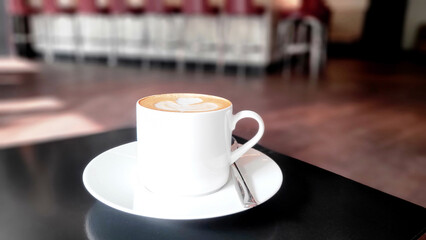 Cup of coffee on black table in cafe. Cappuccino on table in a cafe bar in hotel. White ceramic coffee cup and saucer set. Coffee mug in cafe restaurant. Cafe latte in bar restaurant