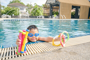 Cute little Asian 6 years old school boy child wear swimming goggles learning to swim with diving...