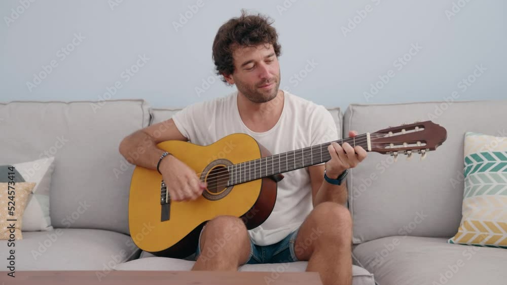 Sticker young hispanic man playing classical guitar sitting on sofa at home