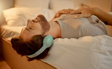 Happy man, streaming a podcast in bed smiling with headphones at home. Young guy listening to music...