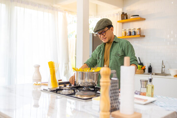 Asian man enjoy cooking pasta putting raw spaghetti in boiling water in saucepan on stove in the kitchen at home. Handsome male having dinner cooking and eating healthy food on holiday vacation