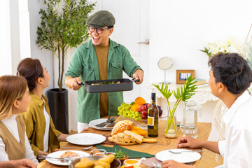 Group of Asian man and woman friends having dinner with drinking wine and talking together on dining table at home. Happy people friendship enjoy reunion meeting celebration party on holiday vacation