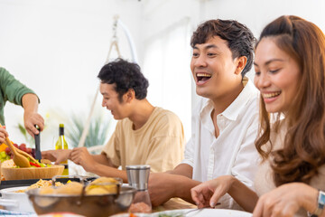 Group of Asian man and woman friends having dinner with drinking wine and talking together on dining table at home. Happy people friendship enjoy reunion meeting celebration party on holiday vacation