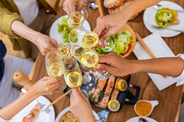Group of Cheerful Asian man and woman friends toasting wine glasses while having dinner together at home. Happy male and female reunion meeting event celebrating party on holiday vacation