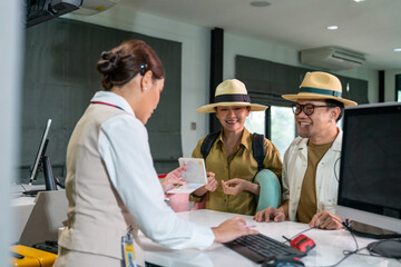 Happy Asian couple man and woman walking to airline ground staff at check in counter and get boarding pass ticket in airport terminal. Airline service business and airplane transportation concept