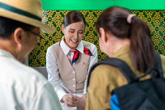 Happy Asian Couple Man And Woman Walking To Airline Ground Staff At Check In Counter And Get Boarding Pass Ticket In Airport Terminal. Airline Service Business And Airplane Transportation Concept