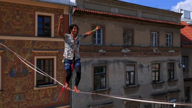 man balances on tight rope, a view of the city from height. Brave Man Slacklining , highlining above people . Nature Adventure and leisure sport . Mountain Balance Extreme Hiker Walking Happy, aerial.