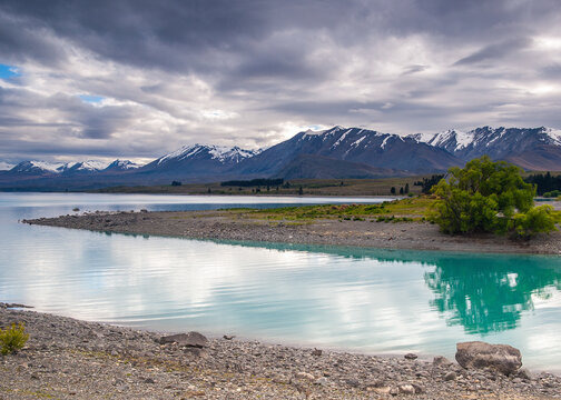 Tranquil turquoise lake surrounded by snow-capped mountains and dramatic clouds in a scenic landscape. - Powered by Adobe