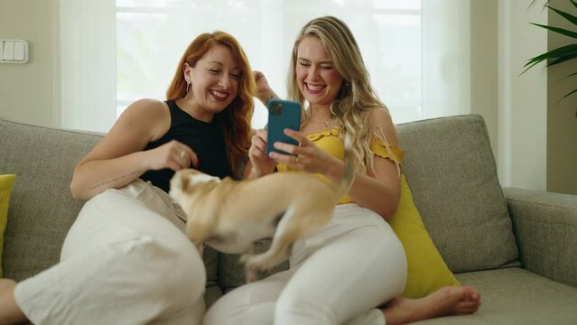 Two women making selfie by smartphone sitting on sofa with chihuahua at home