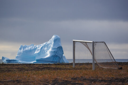 A striking iceberg near a soccer goal on barren tundra, showcasing Greenland's unique and remote scenery.
