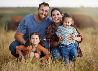 Portrait of happy family on a countryside farm field with cows in the background. Farmer parents...