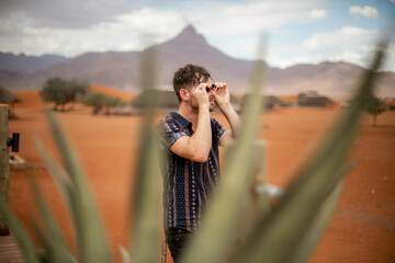 male traveler looking through binoculars in desert safari of namibia africa - obrazy, fototapety, plakaty